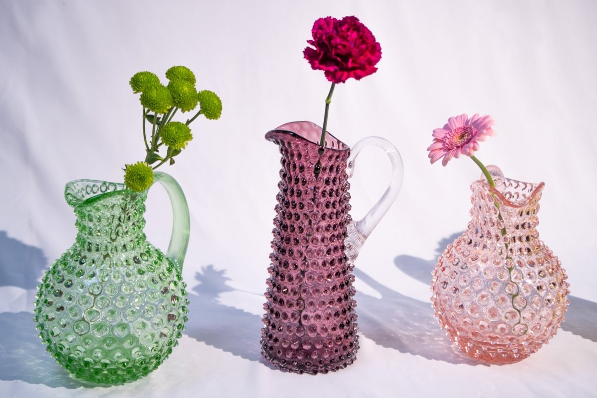 Underlay Violet Hobnail Jug Tall surrounded by products from the Hobnail collection and flowers, on a white fabric and background