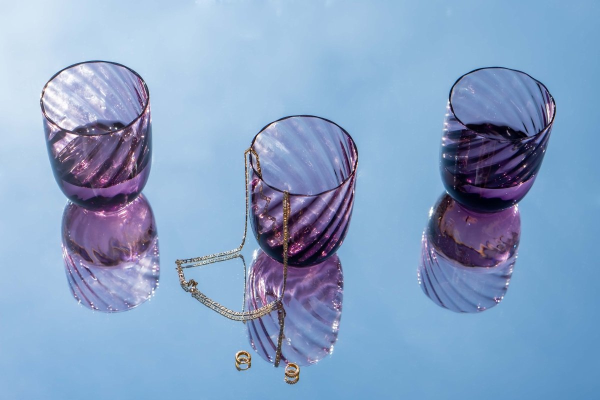 Violet Marika Tumblers on a mirror reflecting the sky and accompanied by gold jewellery
