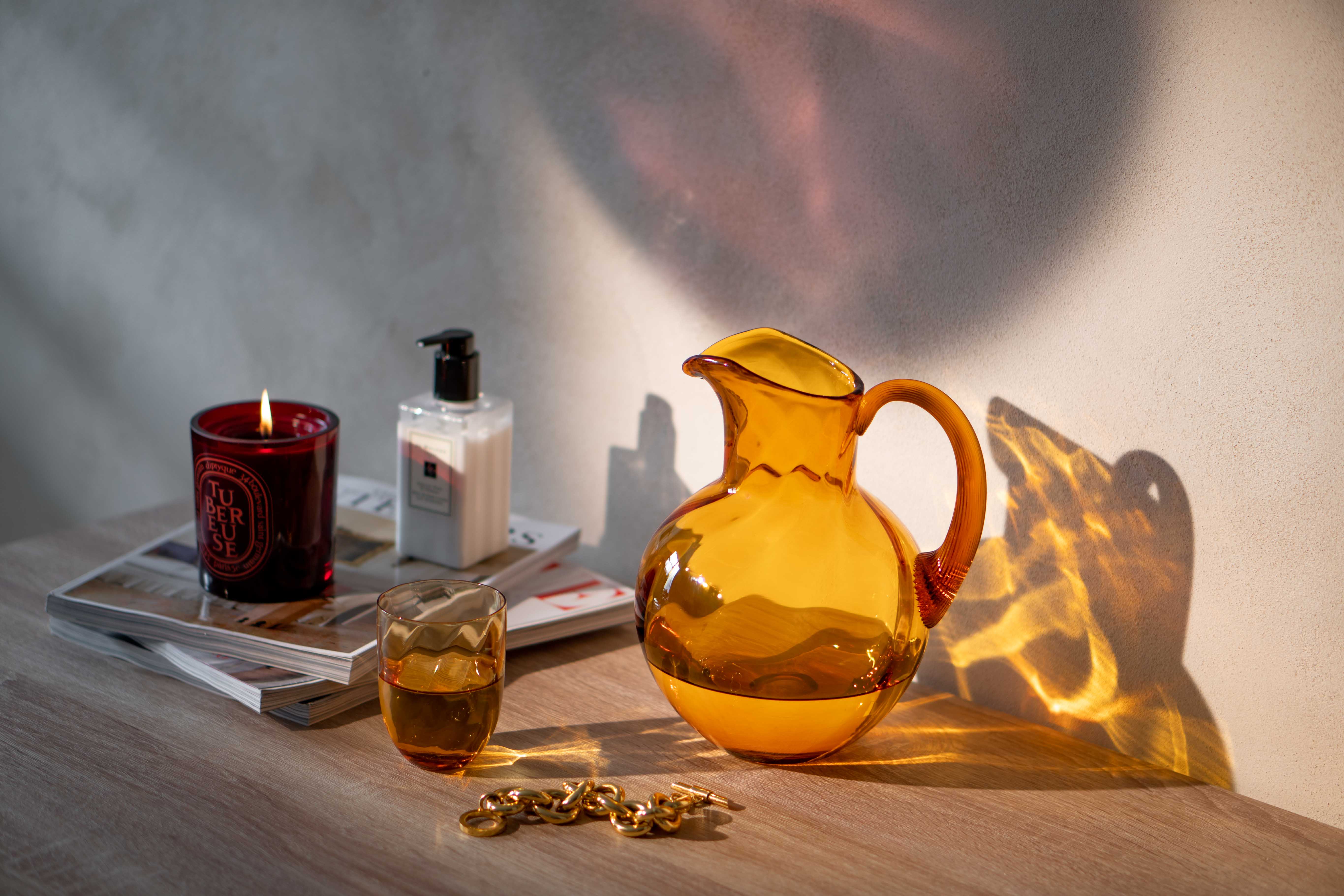 Amber Glass Jug with a matching tumbler on a table with a red candle and a handcream..