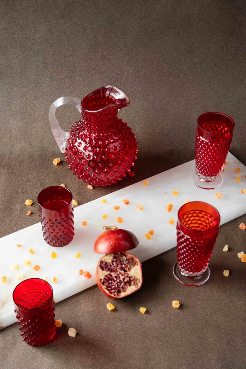 Underlay Garnet Hobnail Jug surrounded by products from the Hobnail collection and fruit on a black background